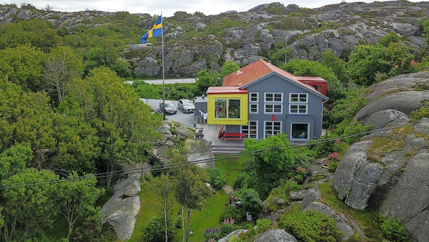 A colorful house with a red roof, surrounded by lush greenery and rocky terrain. - Lådfabriken (Hälleviksstrand)