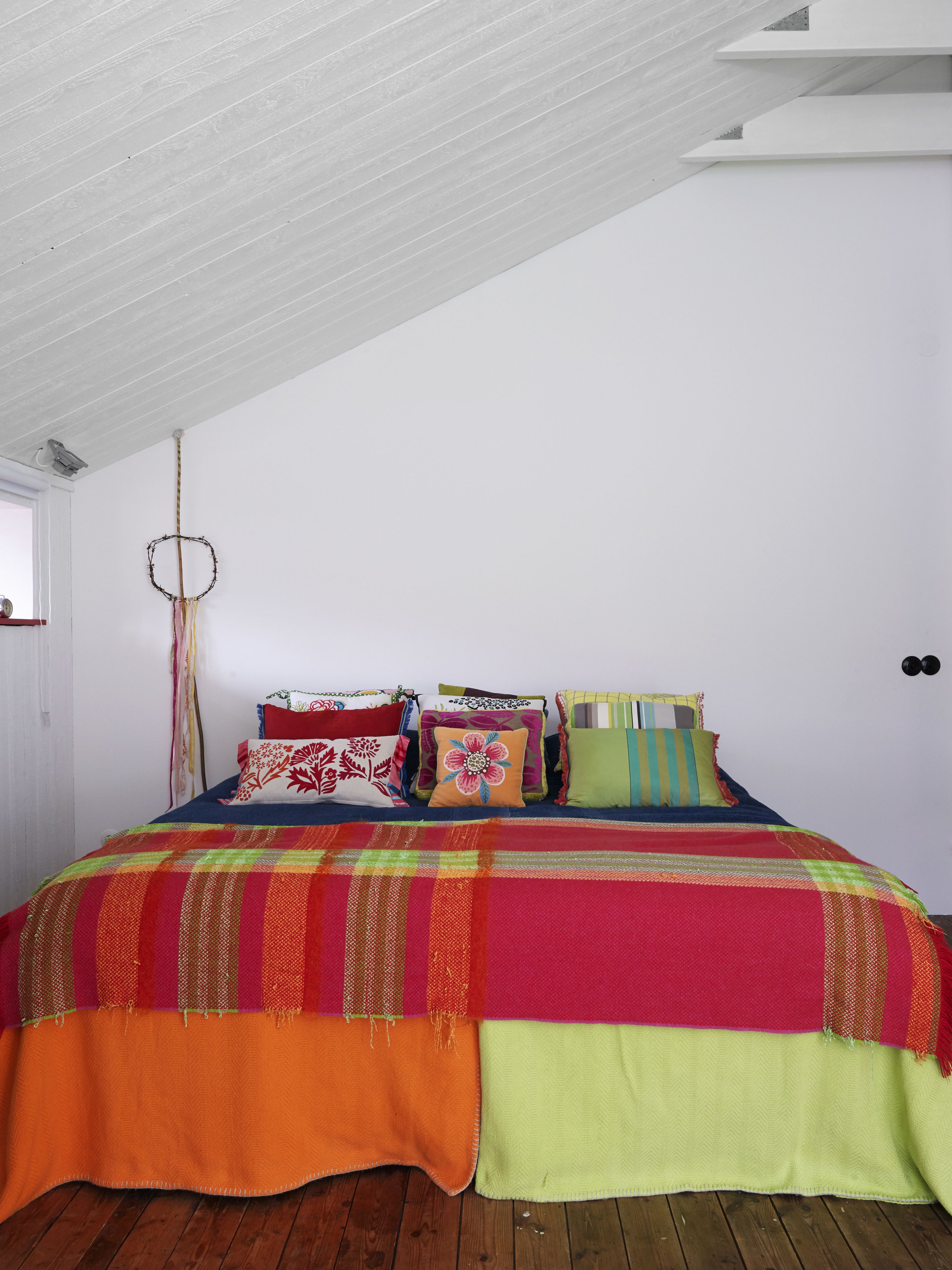 Un dormitorio con techo inclinado, una cama con ropa de cama colorida y un atrapasueños en la pared.