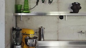 A kitchen with stainless steel countertops, a yellow stand mixer, a blender, and a metal wall-mounted lamp. - Lådfabriken (Hälleviksstrand)