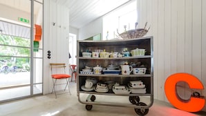 A room with a metal cart filled with various kitchenware, a red chair, and a large orange decorative piece. - Lådfabriken (Hälleviksstrand)