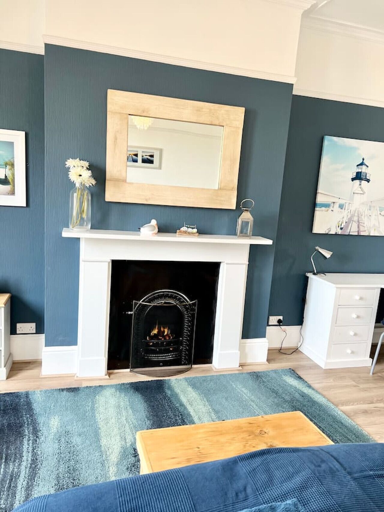 A living room with a fireplace, a mirror above it, a white dresser, and a blue sofa.