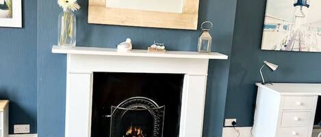 A living room with a fireplace, a mirror above it, a white dresser, and a blue sofa.