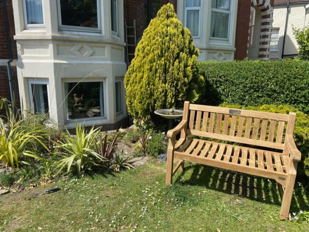 Een houten bankje in een tuin met een kleine boom en een vogelbad.
