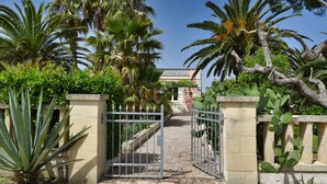A gated entrance with a gravel path leading to a building with a balcony. - Beautiful Villa with pool in the green of Salento, 110 sqm, quiet and luxurious (Cutrofiano)