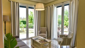 A living room with a sofa, armchair, and coffee table, a lamp, and a view through large sliding glass doors to an outdoor area with chairs and greenery. - Beautiful Villa with pool in the green of Salento, 110 sqm, quiet and luxurious (Cutrofiano)