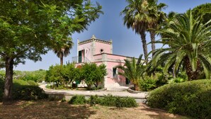 A pink building with a tower, surrounded by palm trees and greenery. - Beautiful Villa with pool in the green of Salento, 110 sqm, quiet and luxurious (Cutrofiano)