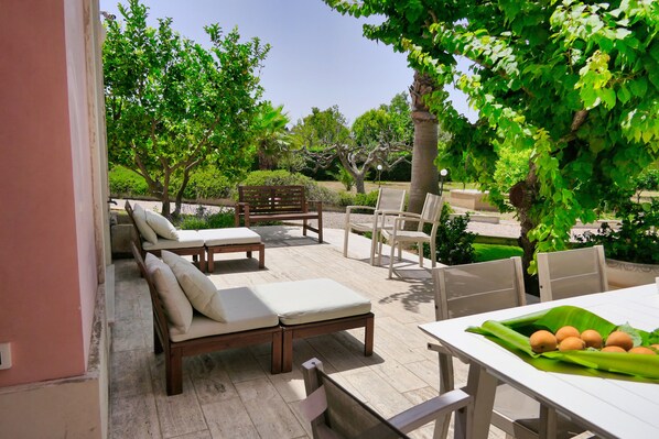 An outdoor patio with lounge chairs and a table, surrounded by greenery and trees.