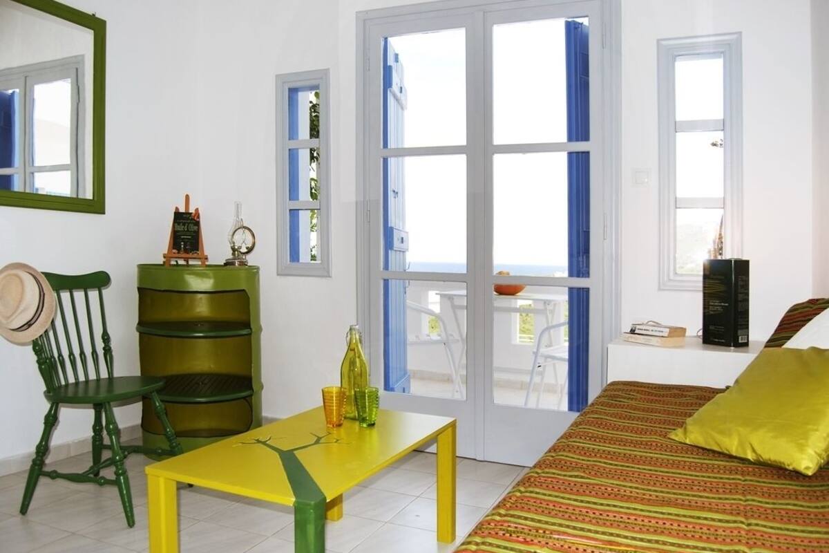 Una habitación con una cama, una mesa amarilla, una silla verde, un armario verde y una ventana con cortinas azules.