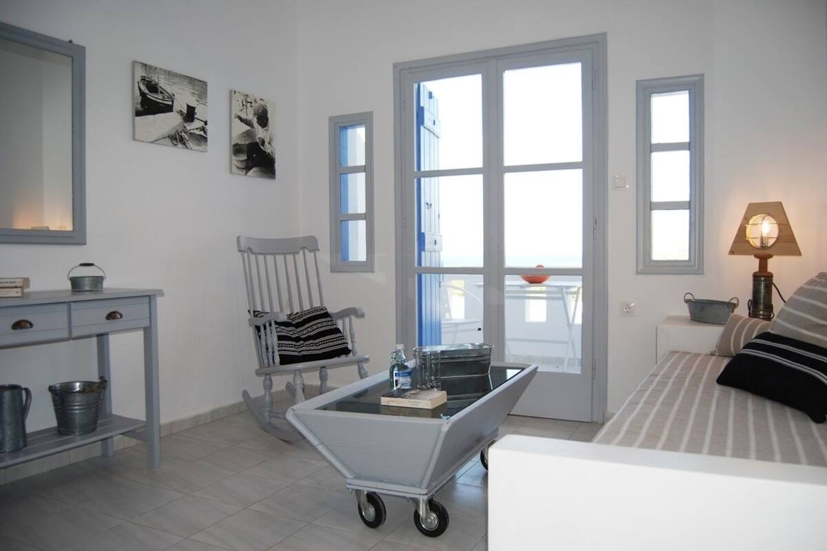 Una habitación con cama, una silla, una mesa con lámpara y vistas a través de una puerta.