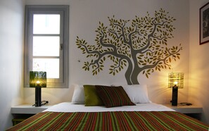 A bedroom with a bed, pillows, a window, and a wall mural of a tree. - Milatos Village Cretan Agrotourism Hotel (Agios Nikolaos)