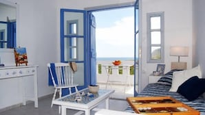 Ein Zimmer mit Bett, Tisch, Stuhl und Blick auf das Meer durch eine offene T ür.