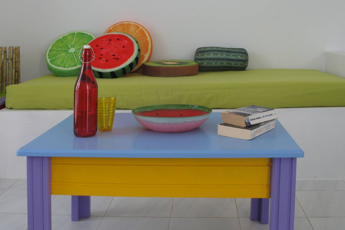 Una mesa colorida con un tazón de sandía, una botella roja y libros.