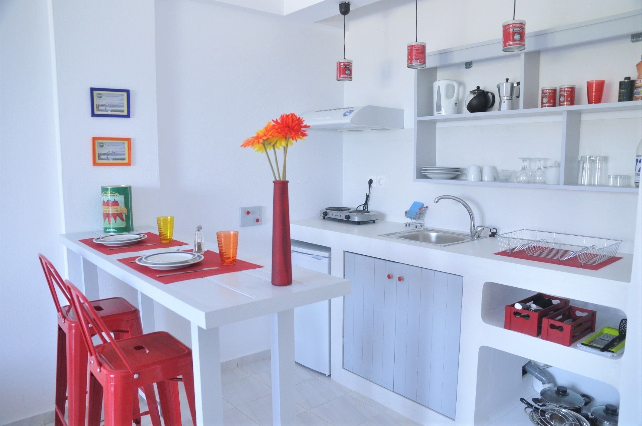 A modern kitchen with white cabinets, a sink, and a dining area with red chairs.