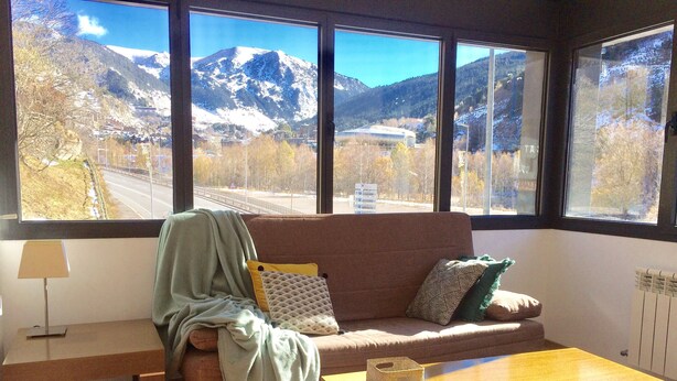 Un salón con sofá, una mesa de centro y vistas a un paisaje montañoso a través de amplios ventanales.