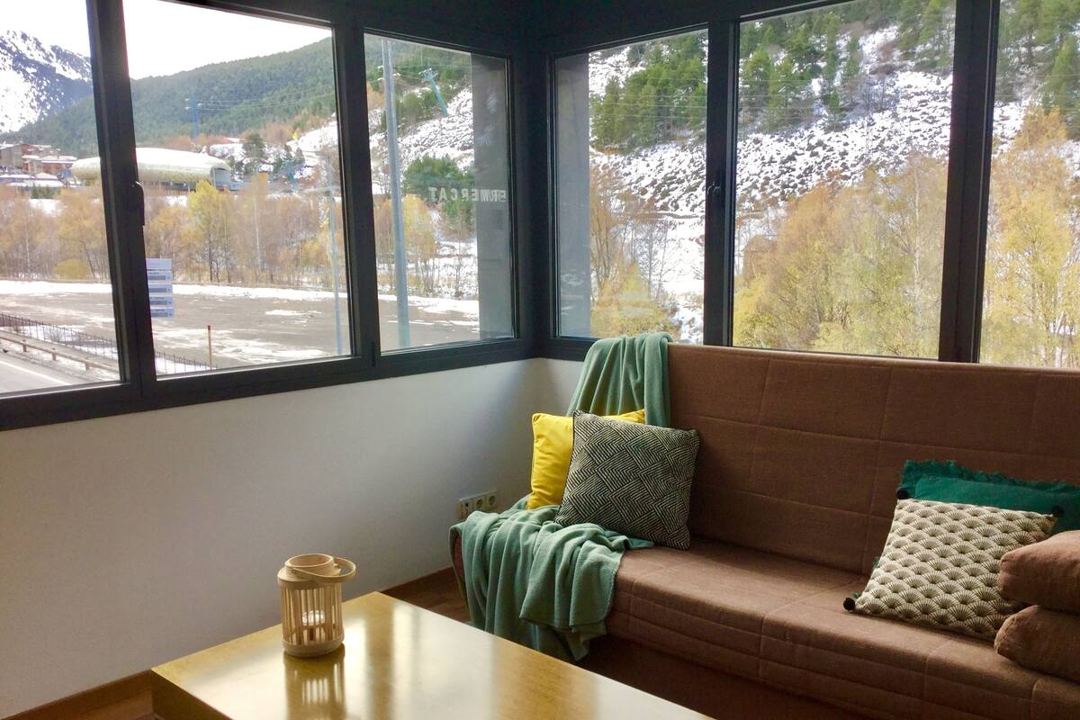 A room with a large window, a brown sofa, a small wooden table, and a lantern.