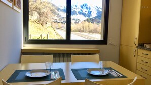 Una mesa de comedor con dos sillas, una ventana con vistas a la montaña y una zona de cocina con armarios.