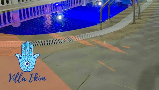 Piscina esterna con recinzione bianca e sedie blu, immersa nel verde e circondata da palme.