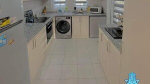 Cucina con mobili bianchi, lavatrice, forno a microonde e lavandino.