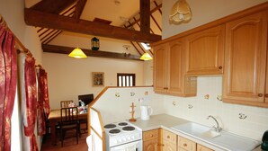 A kitchen with wooden cabinets, a white stove, and a sink. There is a dining table with chairs in the background. - The Granary at Todds House Farm  (Stockton on Tees)