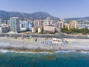 A coastal cityscape with modern high-rise buildings, a beach with sun loungers, and clear blue waters. - Doris Aytur Hotel (Alanya)