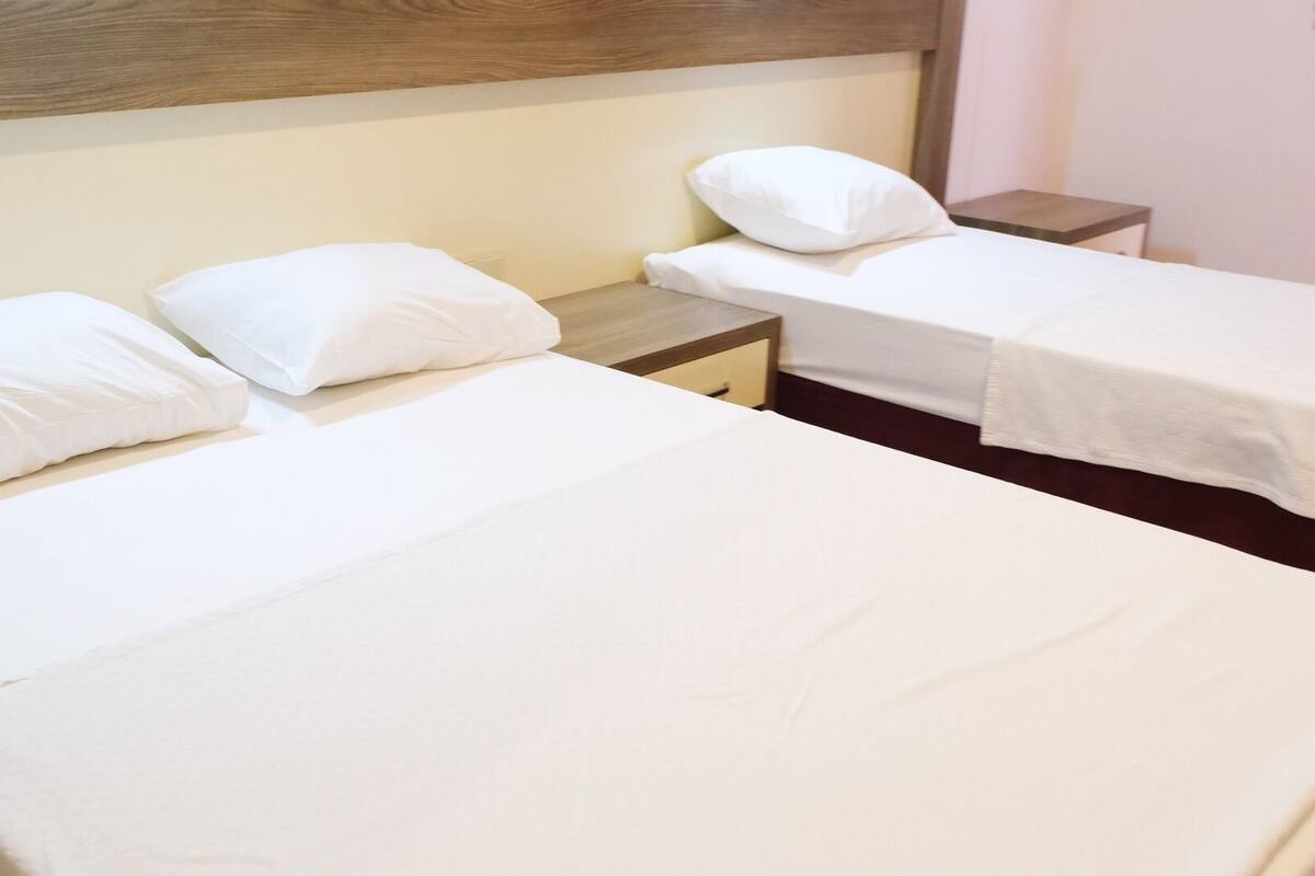 A hotel room with two single beds, each with white bedding and pillows, a wooden headboard, and a small bedside table.