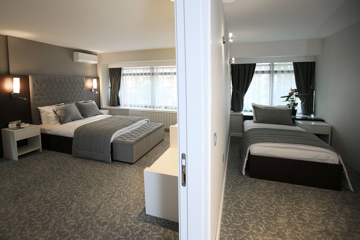 A hotel room with a large bed, a smaller bed, a desk, and a window with curtains.
