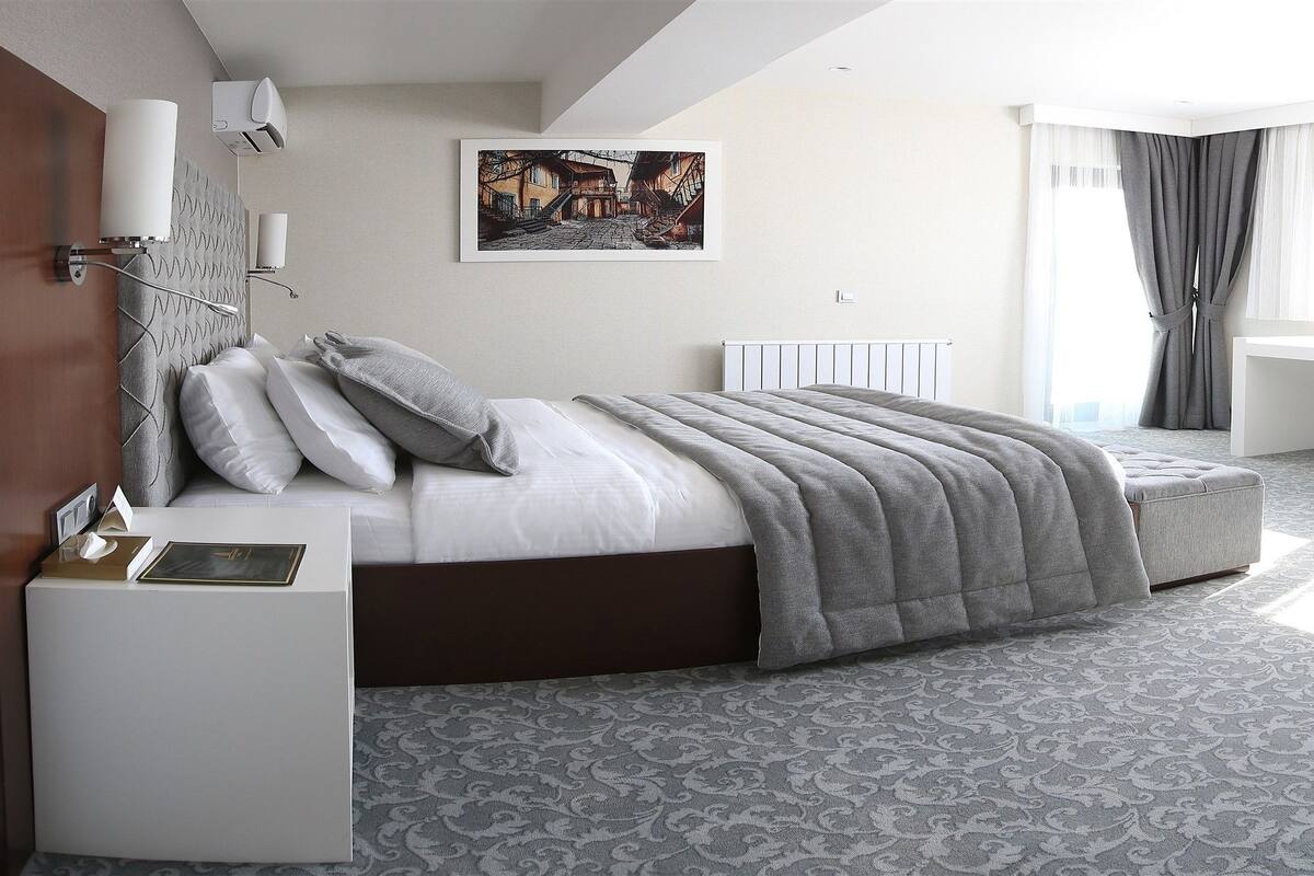 A modern hotel room with a bed, bedside table, desk, and chair.