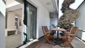 Eine Terrasse im Freien mit Holztisch und -stühlen, einer Glasschiebetür und einem Blumentopf.