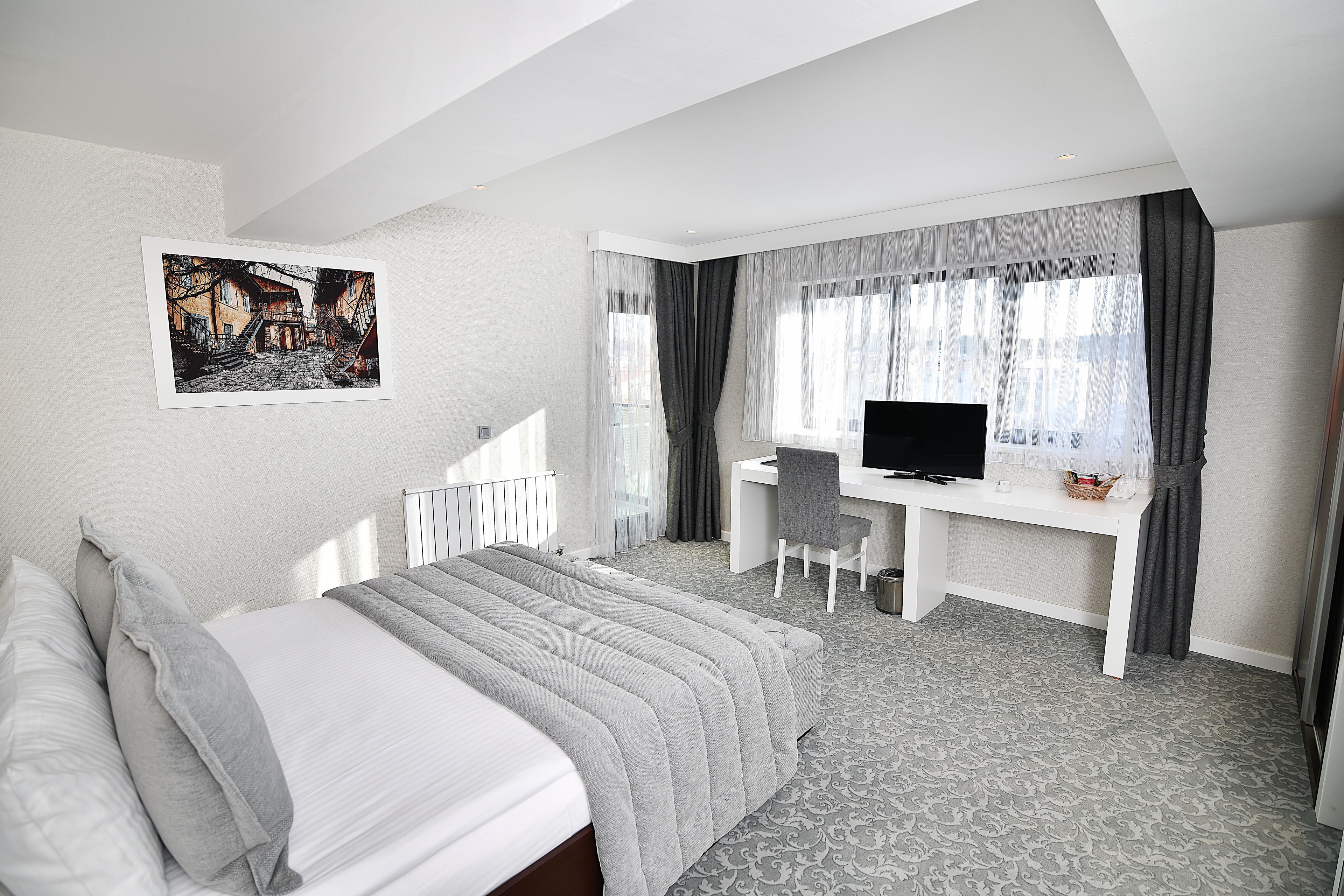 A hotel room with a bed, a desk with a chair, a television, and a picture on the wall.