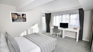 A hotel room with a bed, a desk with a chair, a television, and a picture on the wall.