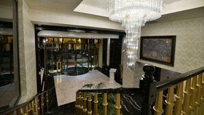 Uma escadaria imponente com um lustre, piso de mármore e vista para um restaurante ou área de refeições.