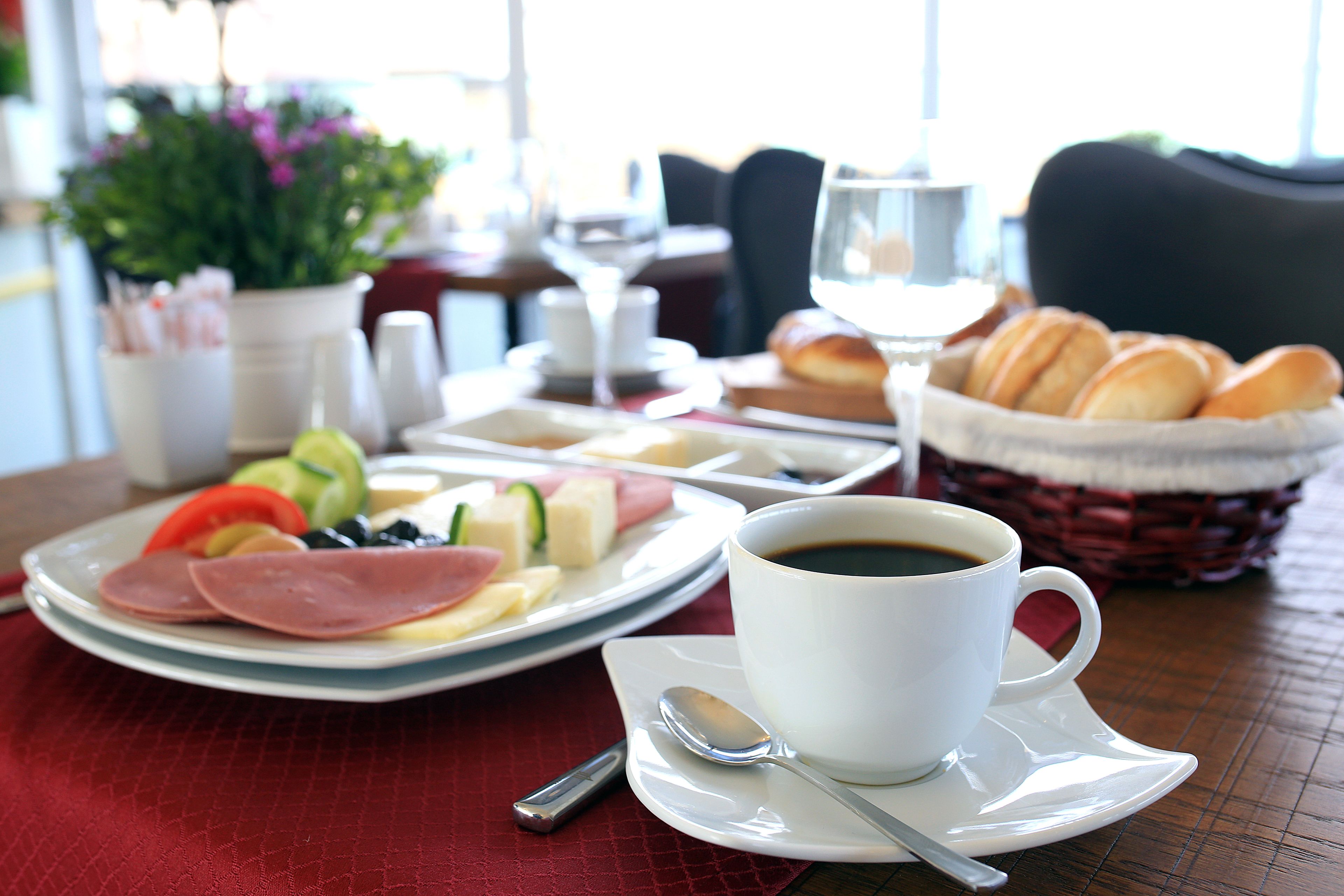 A breakfast setting with a plate of food, a cup of coffee, and a basket of pastries on a table.