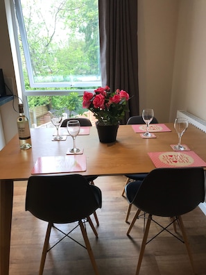 A dining table with two chairs, a potted plant with pink flowers, and two wine glasses.