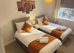 A hotel room with two beds, each with a headboard, pillows, and towels. There is a window with curtains and a view of the outside. - Fabulous with 4 Beds, Town house, sleeps 6, 5 mins from Bracknell Town & Station (Bracknell)