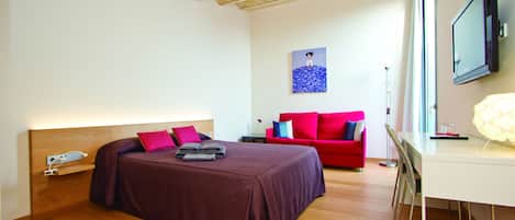 A bedroom with a bed, a desk, a chair, a red sofa, and a painting on the wall.