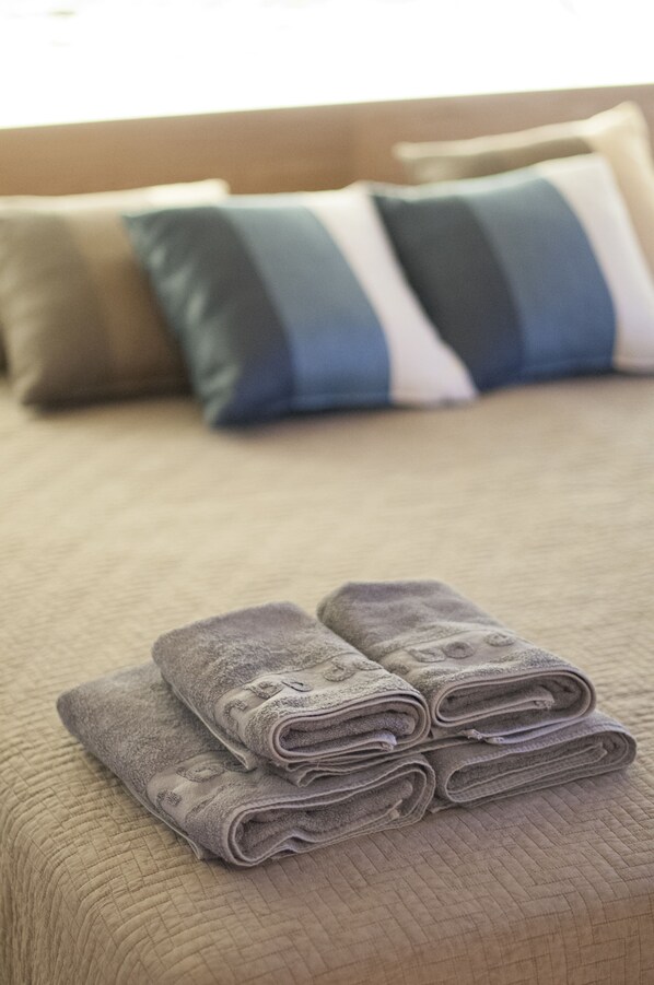 A neatly made bed with a folded gray towel and a striped pillow in the background. - Hotel Can Bo de Pau (Salt)