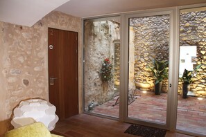A room with a stone wall, a wooden door, and a sliding glass door leading to an outdoor area with a stone wall and potted plants. - Hotel Can Bo de Pau (Salt)