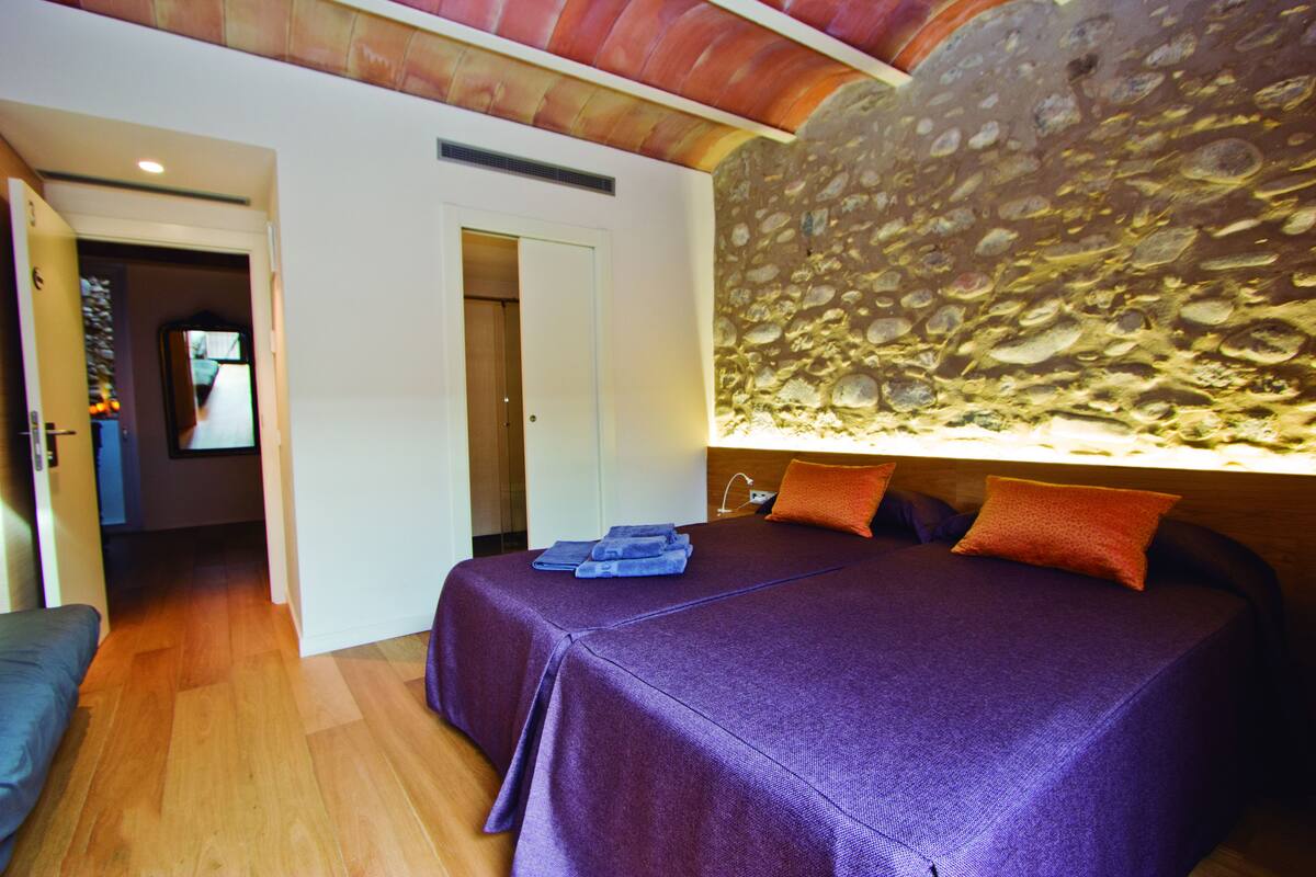 A room with a bed, a stone wall, and a door leading to another room.