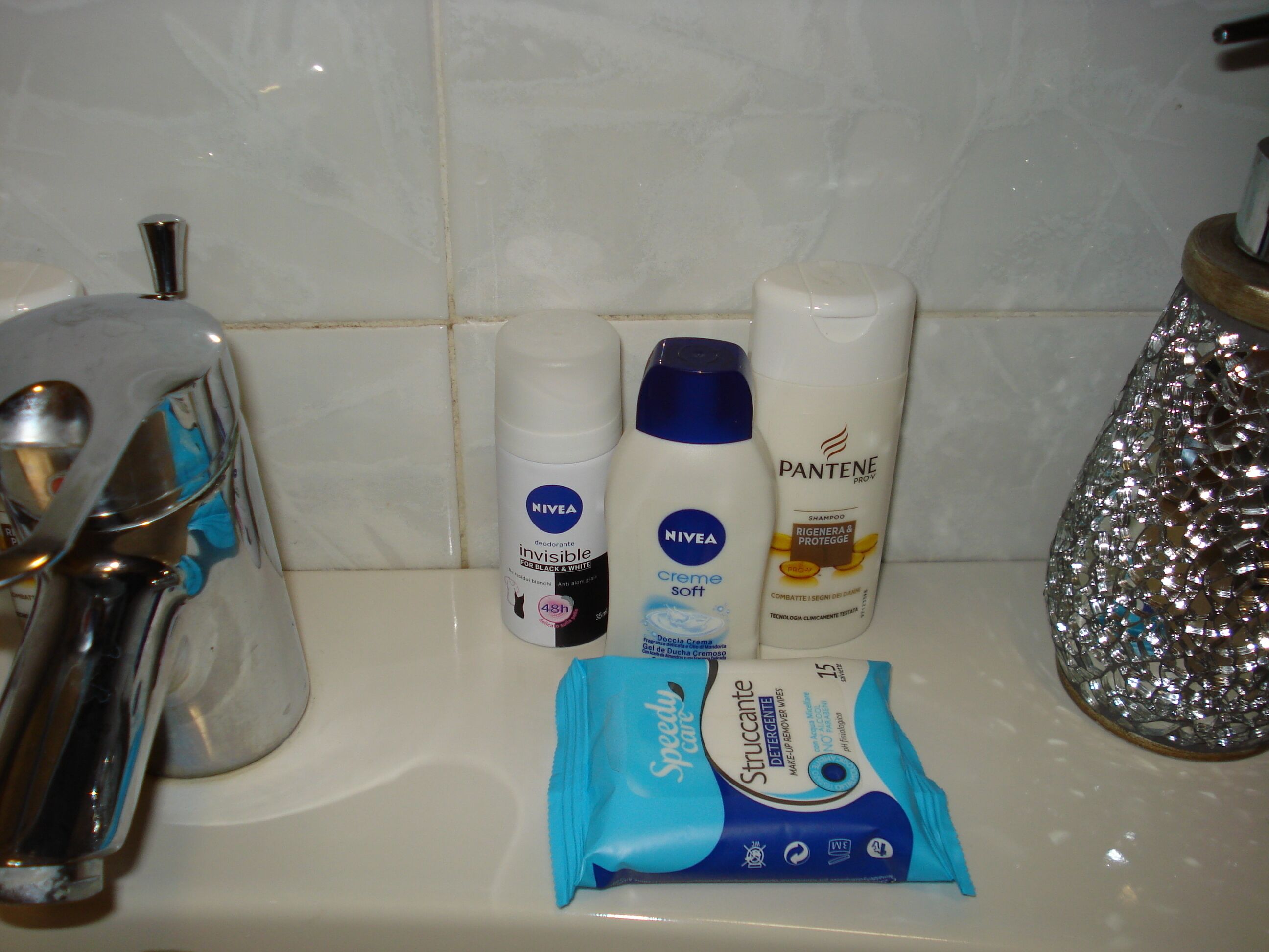 Un lavabo de salle de bain avec des articles de toilette, notamment un déodorant Nivea, un shampooing Pantene et un produit démaquillant Speedy Care.