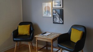 Une pièce avec deux chaises noires dotées de coussins jaunes, une petite table en bois et un luminaire suspendu jaune.