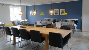 Un espace repas avec une longue table en bois, des chaises noires et des lampes suspendues jaunes.