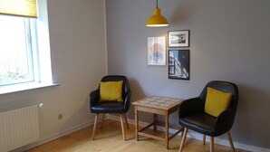 Une pièce avec deux chaises noires dotées de coussins jaunes, une petite table en bois et un luminaire suspendu jaune.