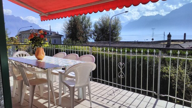 Une terrasse avec une table et des chaises, un auvent rouge et une vue sur la mer et les montagnes.