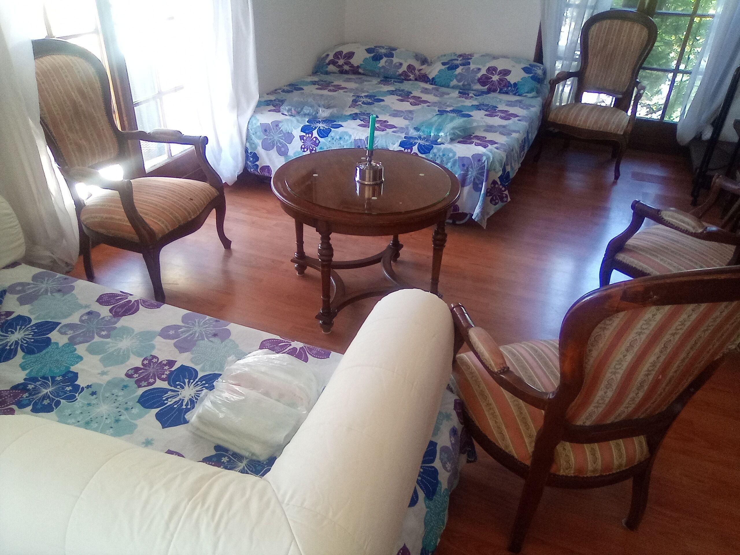 Une pièce comprenant un canapé, deux fauteuils, une petite table ronde et un lit avec une literie à motifs floraux.