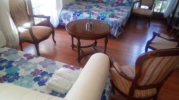 Une pièce comprenant un canapé, deux fauteuils, une petite table ronde et un lit avec une literie à motifs floraux.