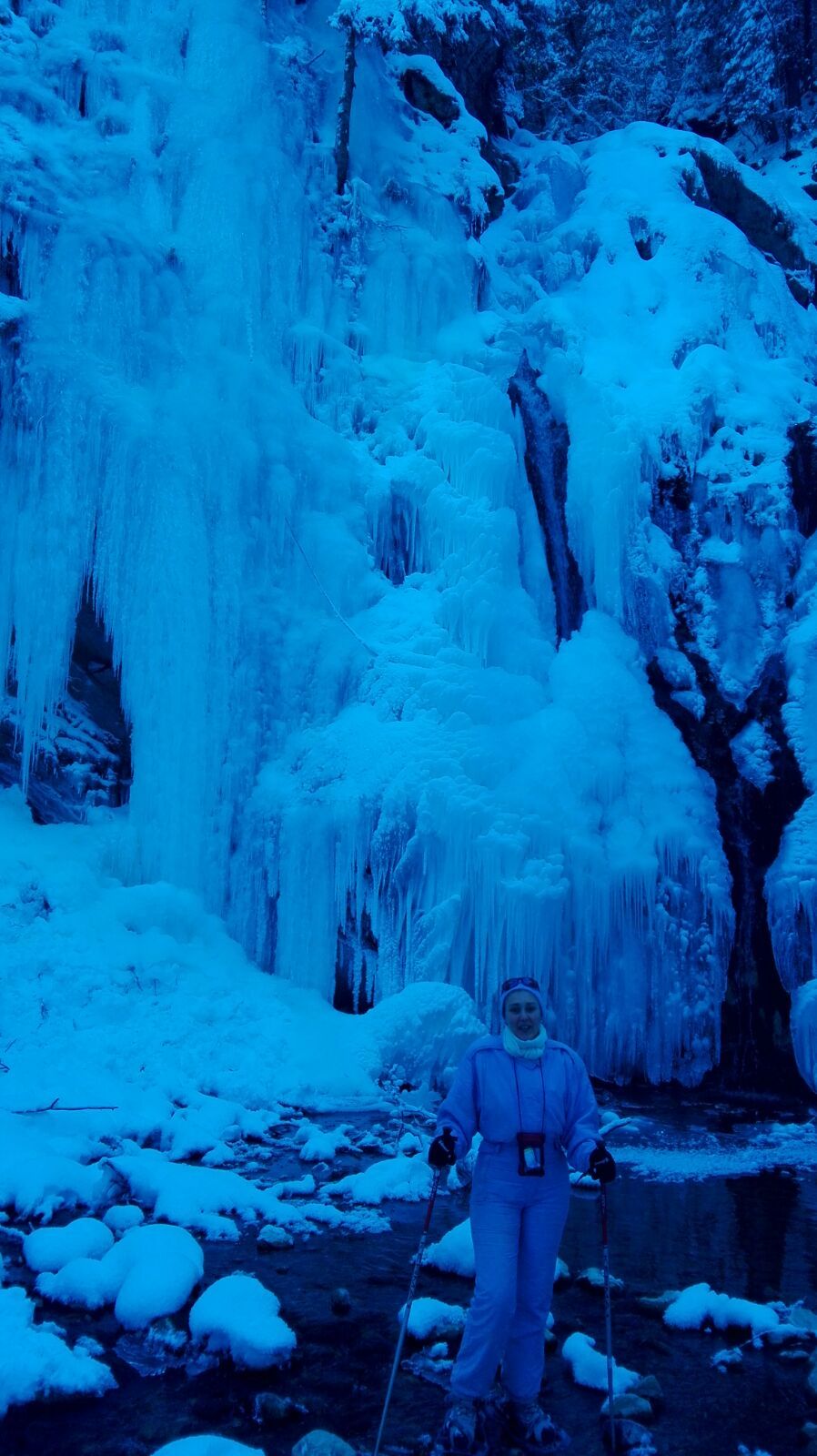 Une personne se tient debout dans un paysage enneigé, avec une cascade en arrière-plan.
