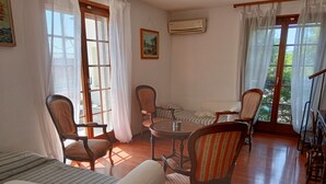 Une pièce avec un plancher en bois, une table ronde et des chaises à rayures. On y trouve un canapé et une fenêtre avec des rideaux.