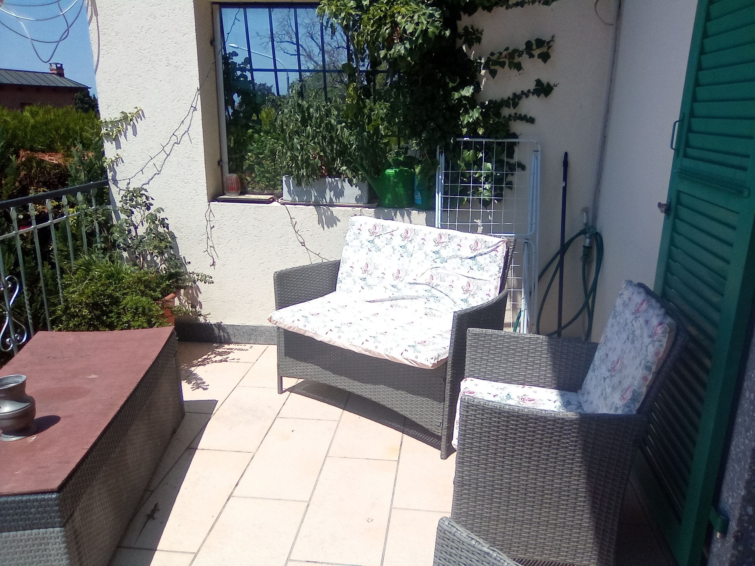 Un patio con mobiliario de mimbre, una mesa y una puerta verde.