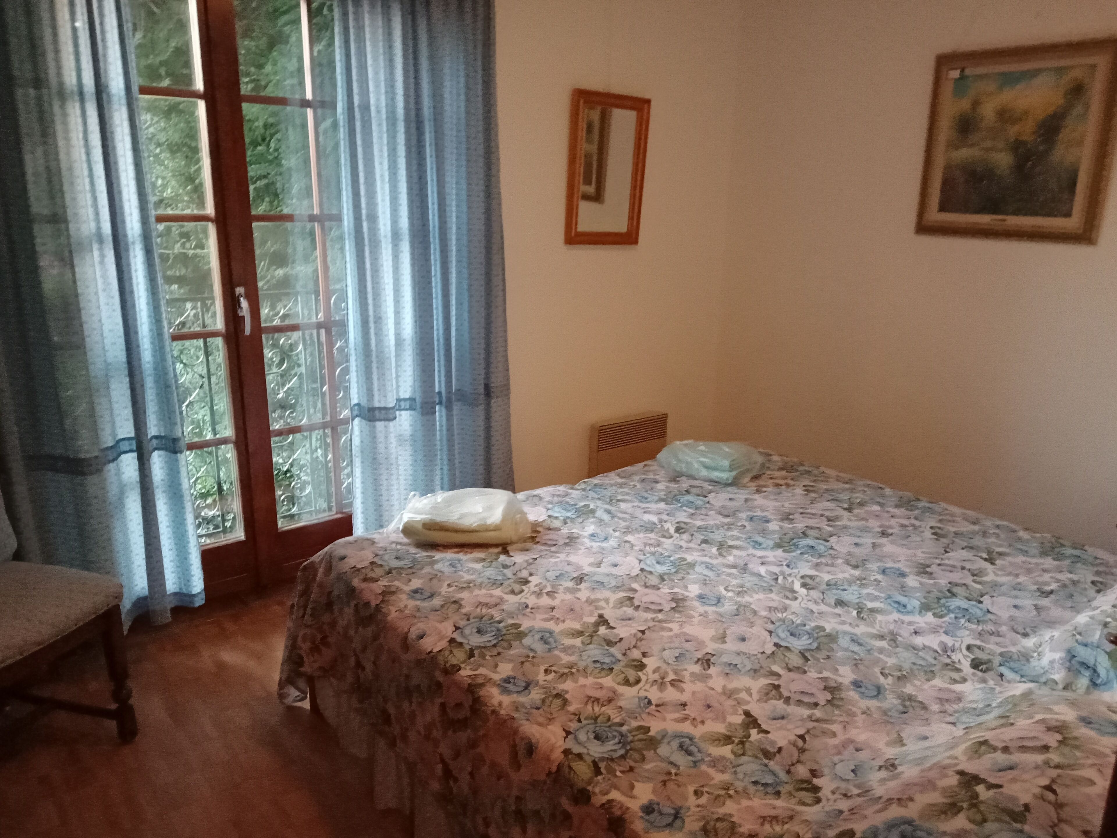 A bedroom with a bed, a chair, a window with curtains, and a painting on the wall.
