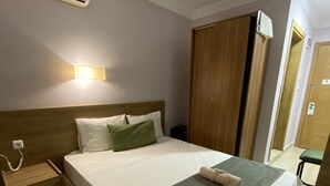 Una cama bien hecha con una manta verde, cabecera de madera, mesita de noche con un teléfono y aire acondicionado de pared.